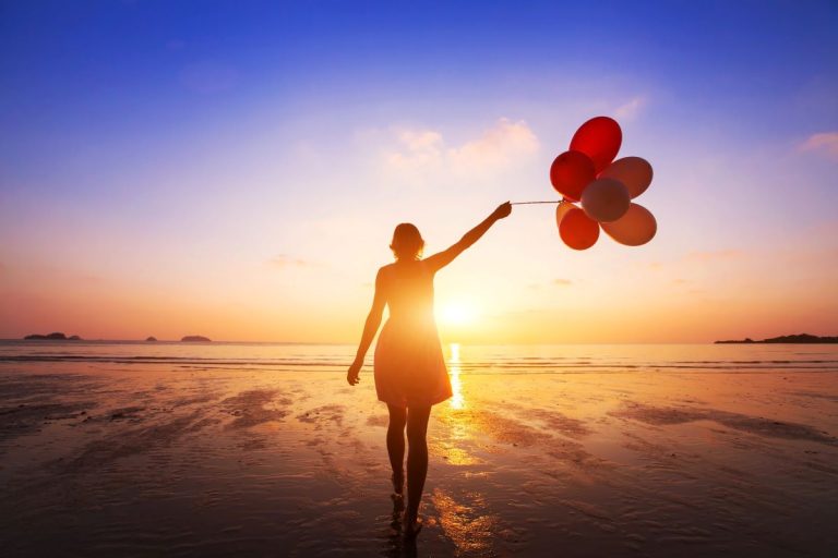 Woman walking into sunset with handful of helium balloons.